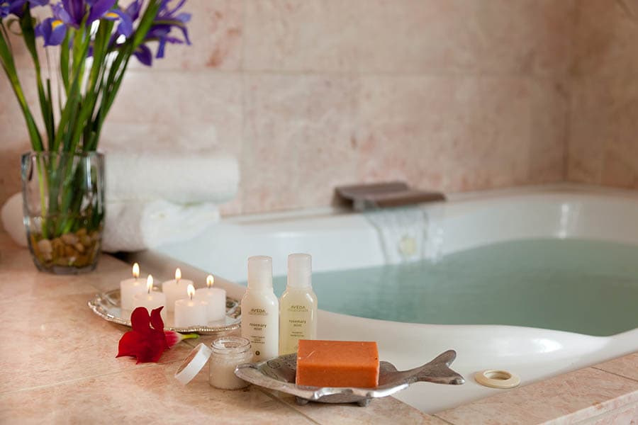 A serene bathroom scene featuring a tub filled with water, candles, toiletries, and fresh flowers.