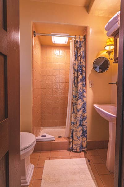 A small, tiled bathroom featuring a shower, toilet, and sink with floral curtains.