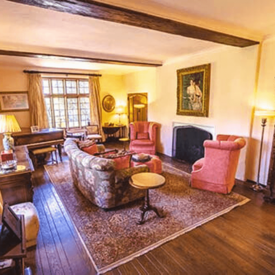Cozy living room with a floral sofa, pink armchairs, and a piano, adorned with warm lighting.