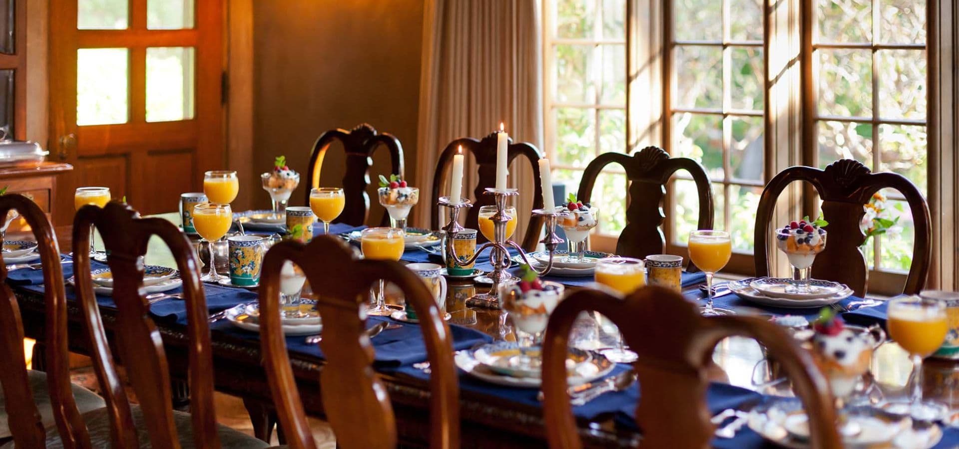 A beautifully set dining table with colorful drinks and desserts, illuminated by natural light from nearby windows.