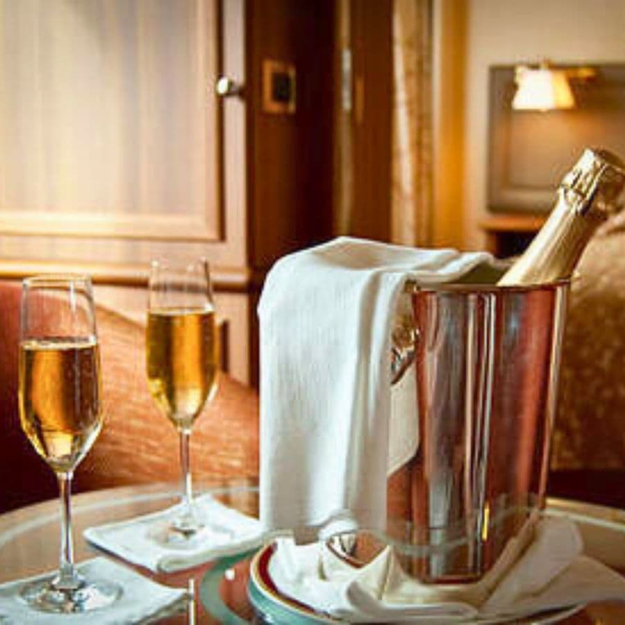 A bottle of champagne in an ice bucket is accompanied by two glasses filled with sparkling wine on a table.