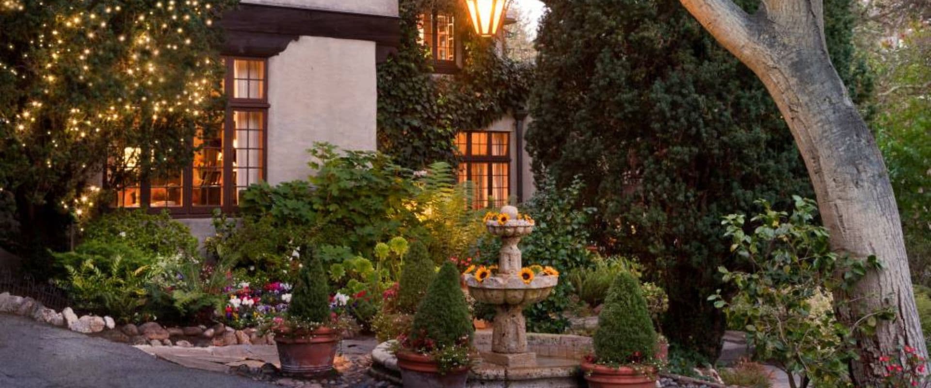 A charming garden with a fountain and decorative lights in front of a house.