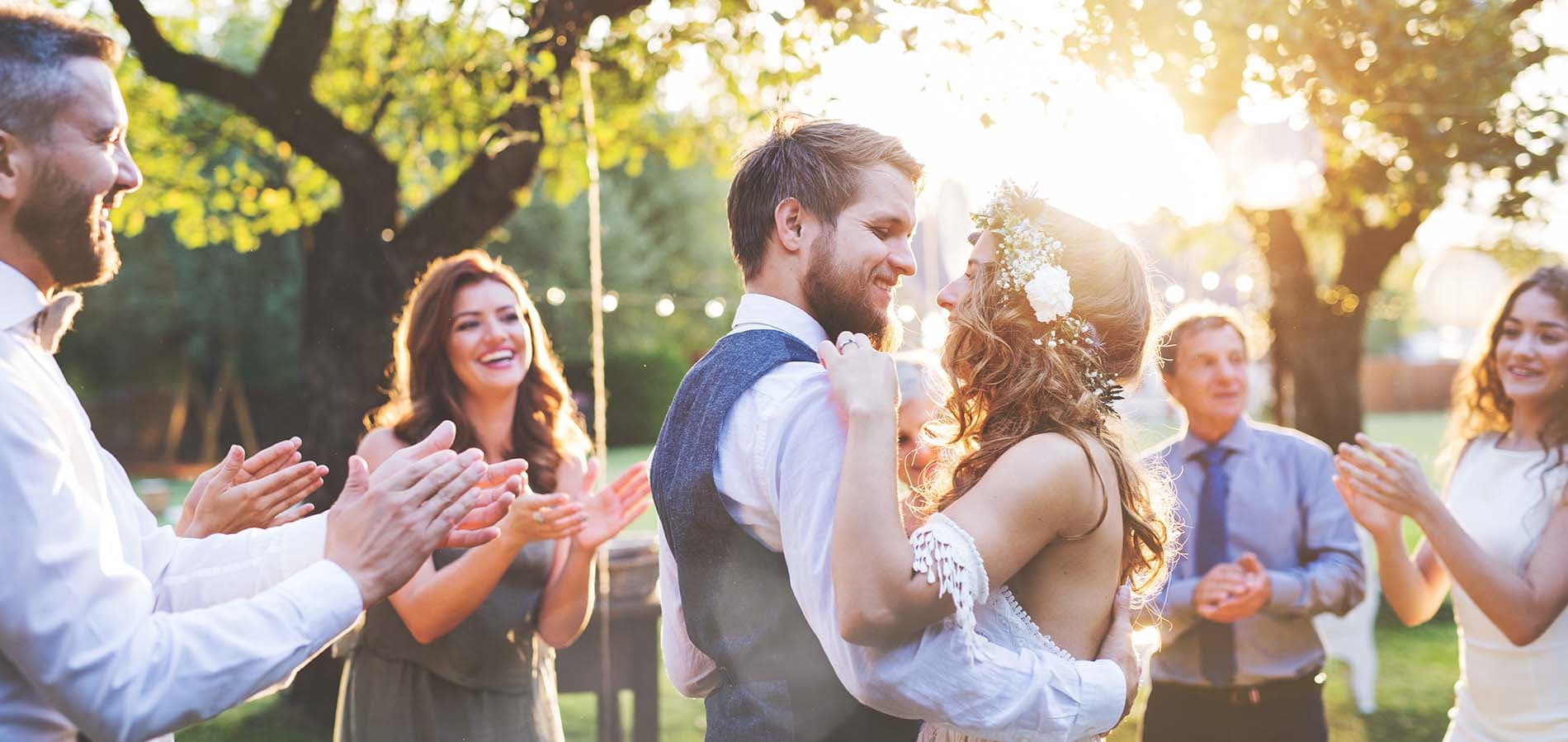 A joyful couple dances together at their wedding while surrounded by smiling friends and family.
