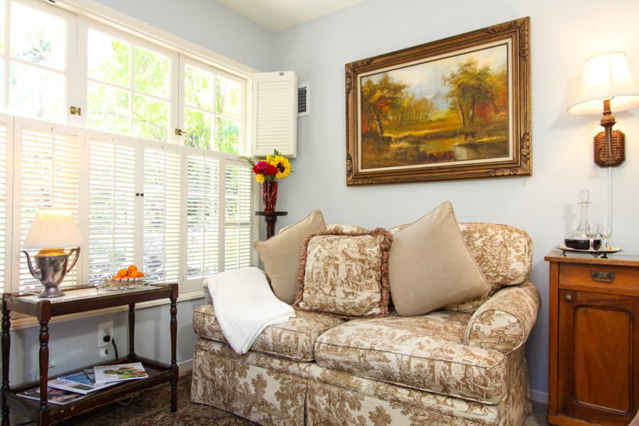 Cozy living room featuring a floral couch, a wooden side table with flowers, and a landscape painting on the wall.