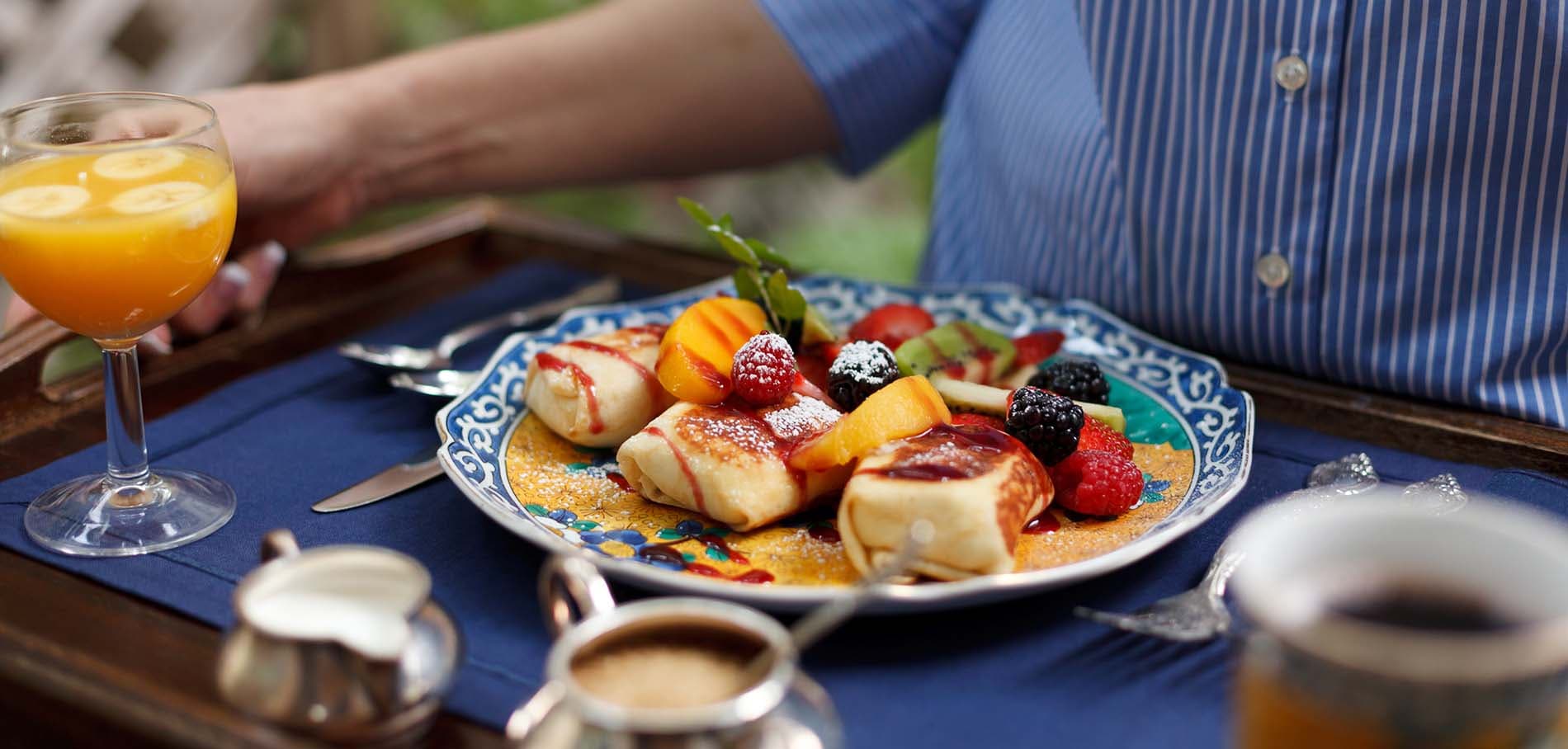 A close-up of a breakfast platter featuring fruit, pancakes, and a glass of orange juice on a blue tablecloth.