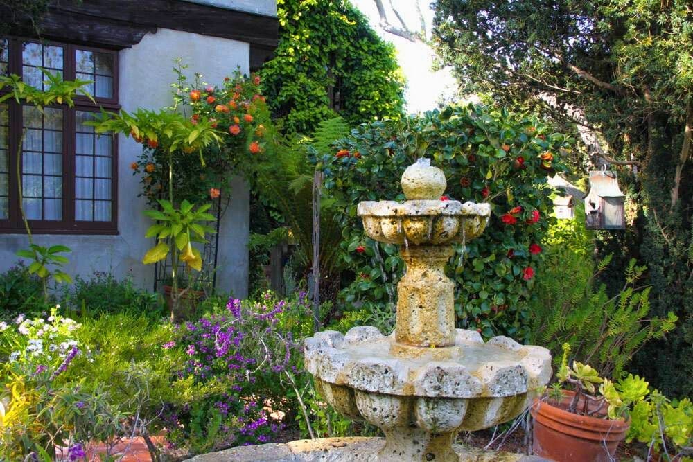 A stone fountain surrounded by lush greenery and blooming flowers in a vibrant garden.