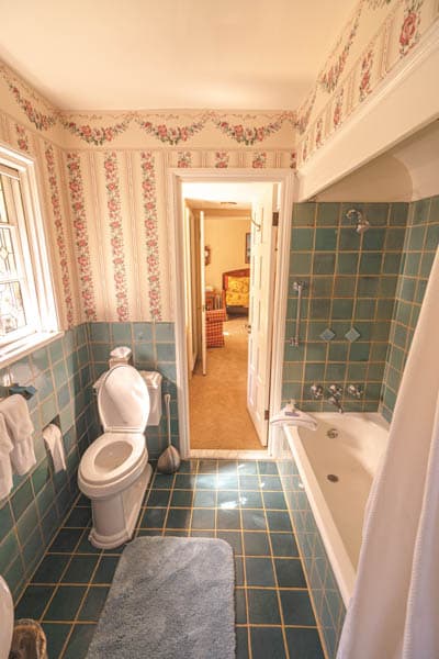 A vintage-style bathroom featuring a toilet, bathtub, and floral wallpaper.