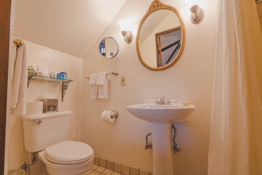 A small bathroom featuring a toilet, sink, mirror, and towel rack with soft lighting.