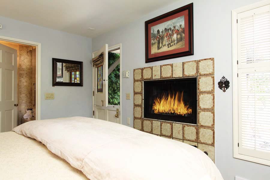 Cozy bedroom featuring a fireplace, framed artwork, and natural light from a nearby window.