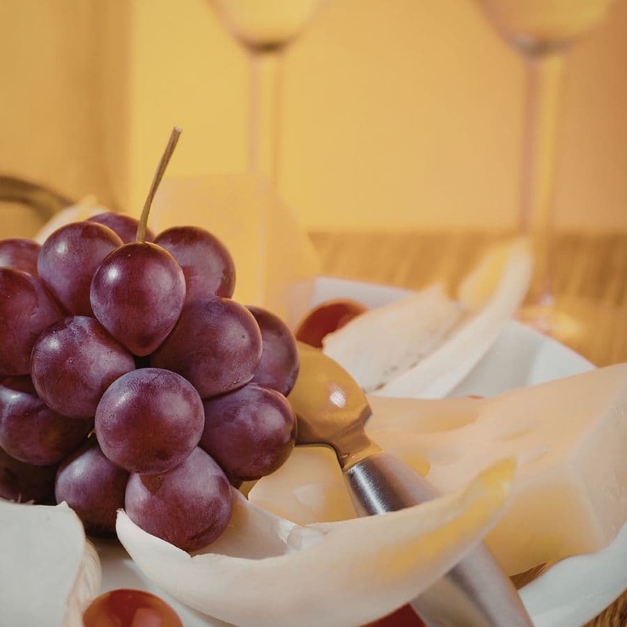 A plate of cheese, grapes, and cherry tomatoes with a serving fork.