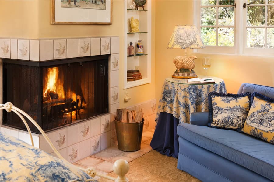 A cozy living room featuring a blue sofa, floral tablecloth, and a lit fireplace.