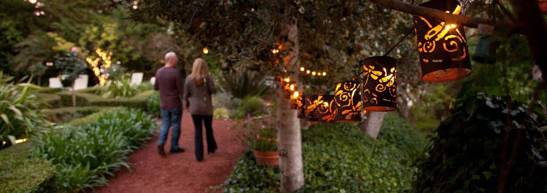 A couple walks along a garden path illuminated by decorative lanterns.