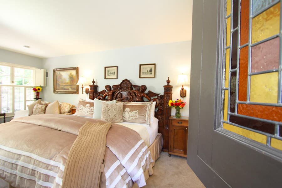 Cozy bedroom featuring an ornate wooden bed, decorative pillows, and a stained glass window.