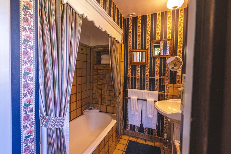A vintage-style bathroom featuring a tub with a shower curtain, decorative wallpaper, and towels on a rack.