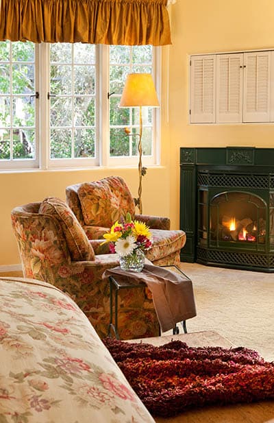 Cozy living space featuring floral armchairs, a warm lamp, a fireplace, and a vase of flowers.