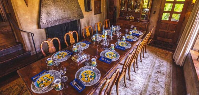 Elegant dining table set with colorful place settings, glassware, and candles in a warm rustic dining room.