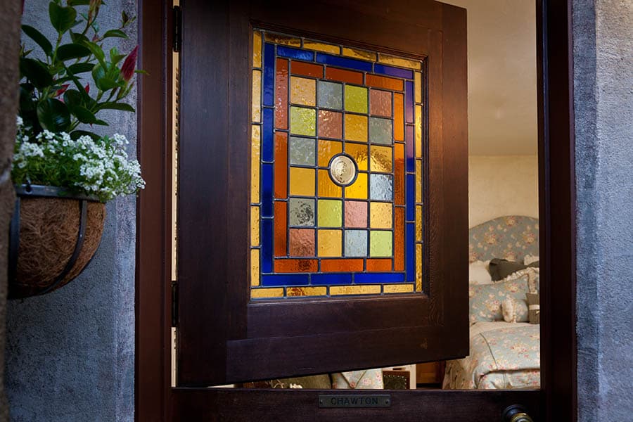 A wooden door partially open, revealing a colorful stained glass panel and a glimpse of a softly decorated room.