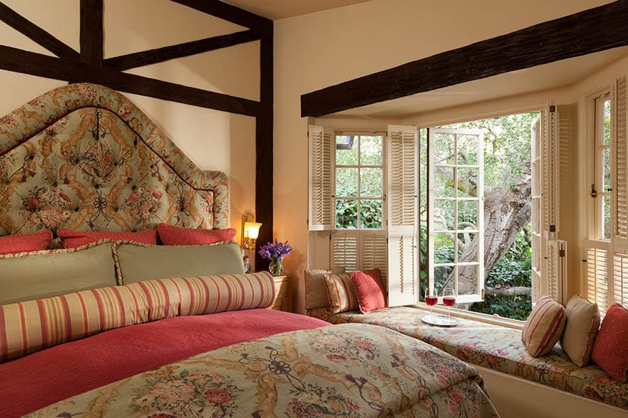 Cozy bedroom featuring a floral bedspread and an open window overlooking a garden.