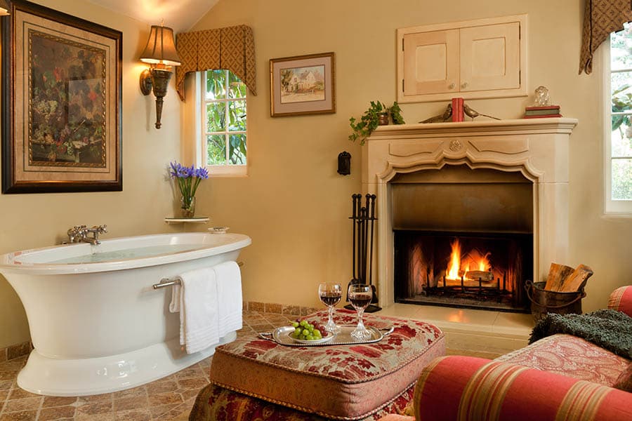 A cozy bathroom featuring a freestanding bathtub, a fireplace, and a small table with wine and snacks.