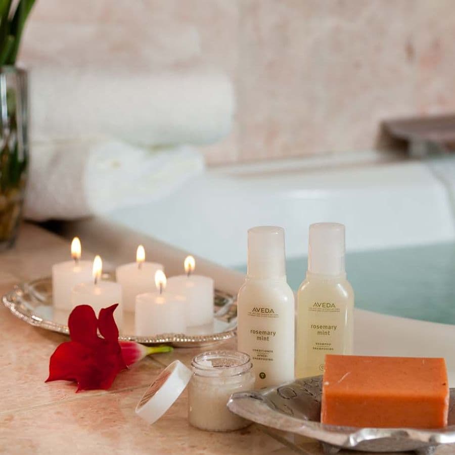 A relaxing spa setup featuring Aveda rosemary mint products, candles, and towels near a bathtub.