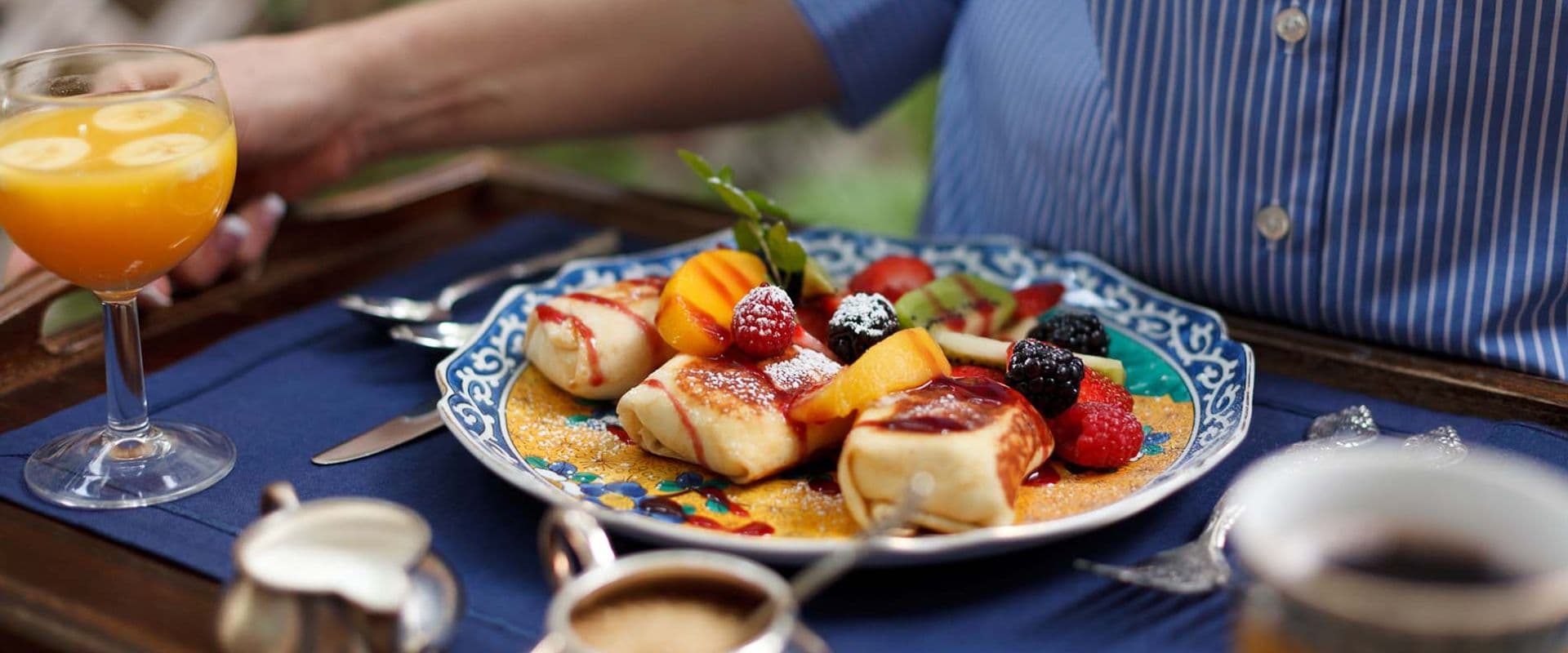 A beautifully arranged breakfast plate featuring pancakes and fresh fruit, accompanied by a glass of orange juice.