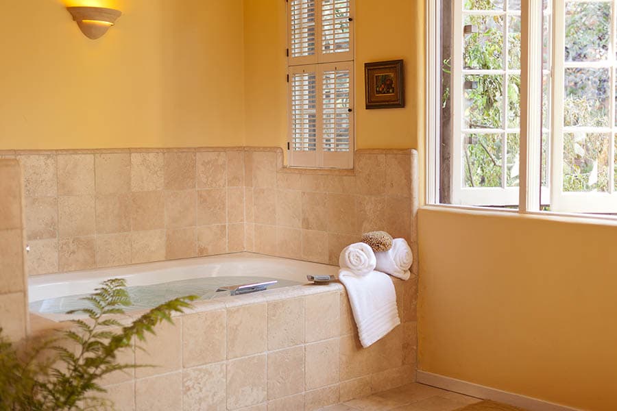 A bright bathroom featuring a tiled jacuzzi, neatly stacked towels, and a large window with natural light.