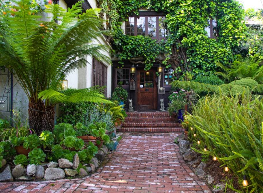 A charming brick pathway leads to a cozy, ivy-covered entrance surrounded by lush greenery.