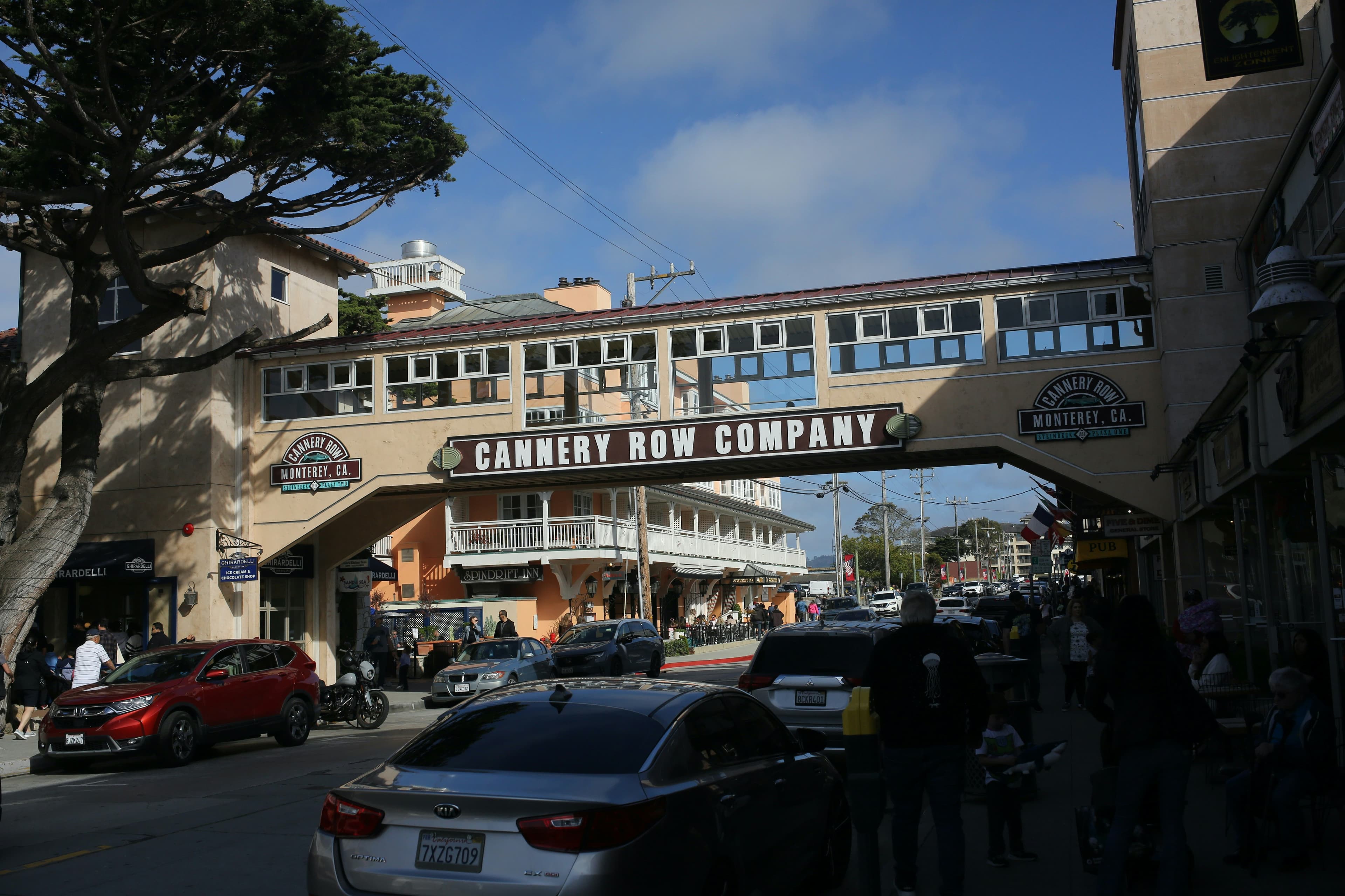 A bustling street scene featuring the Cannery Row Company sign and outdoor shops in a coastal town.