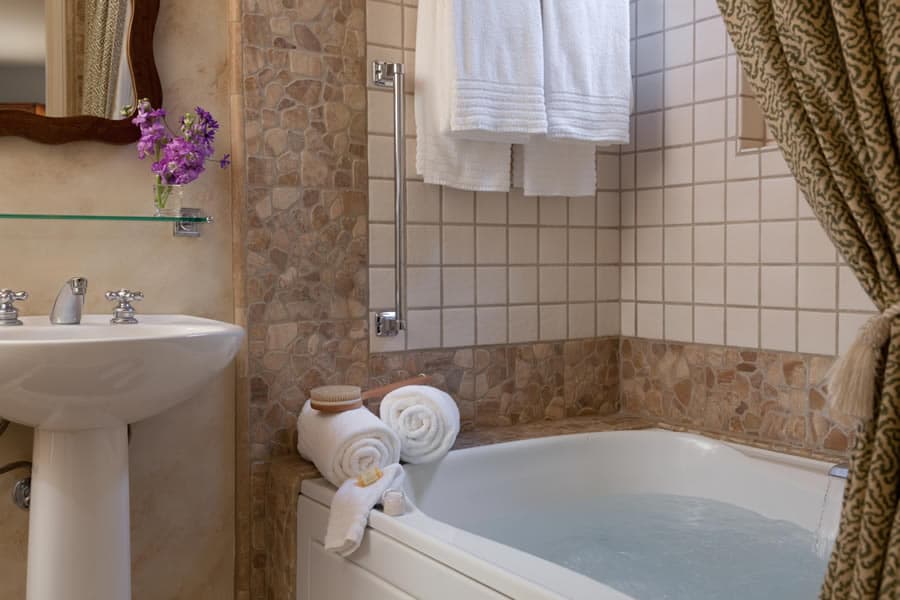 A cozy bathroom featuring a bathtub with water, neatly rolled towels, and a small bouquet of flowers.