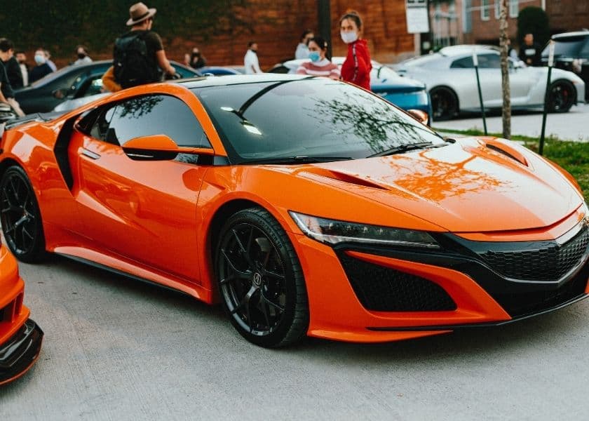 An orange sports car displayed at an outdoor car show.