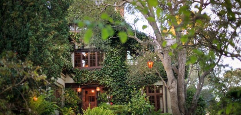 Monterey Inn exterior partially hidden by greenery with ivy covered walls warm lights and trees surrounding the entrance