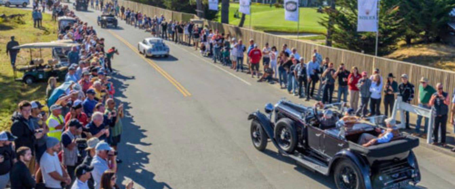 A car festival with old cars driving down a street with onlookers watching