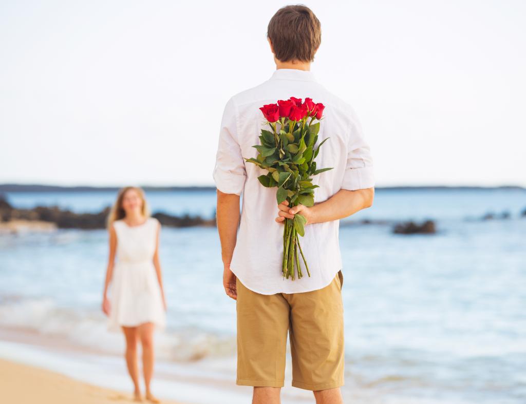 couple at beach with flowers behind his back